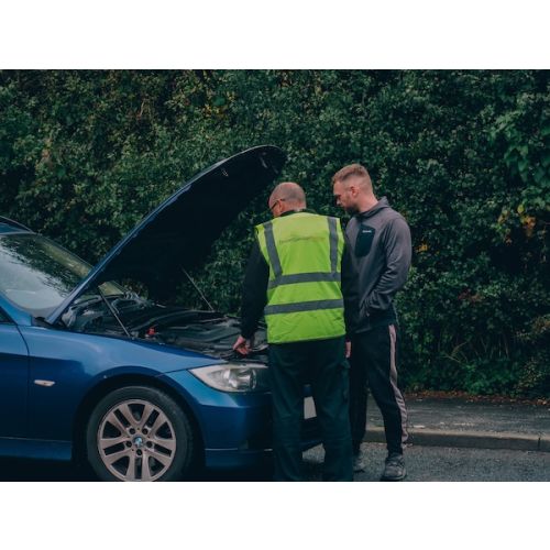 Two men by a broken-down vehicle; one, a Driver Guardain mechanic, assesses the mechanical issue while the other looks on.